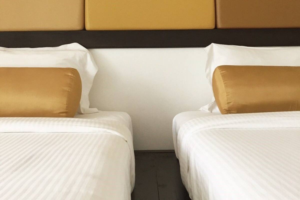 Een hotelkamer met twee bedden, elk voorzien van wit beddengoed en één bruin kussen.