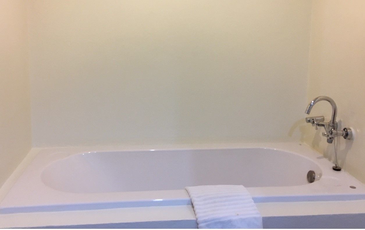 Una bañera estándar con un grifo y una toalla sobre el borde.