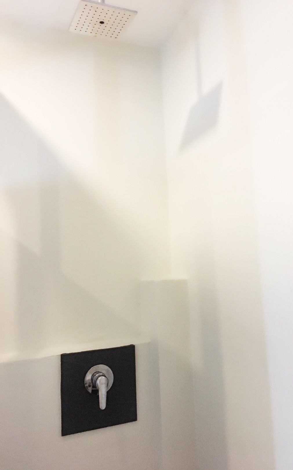 A shower area with a black control panel and a ceiling-mounted showerhead.