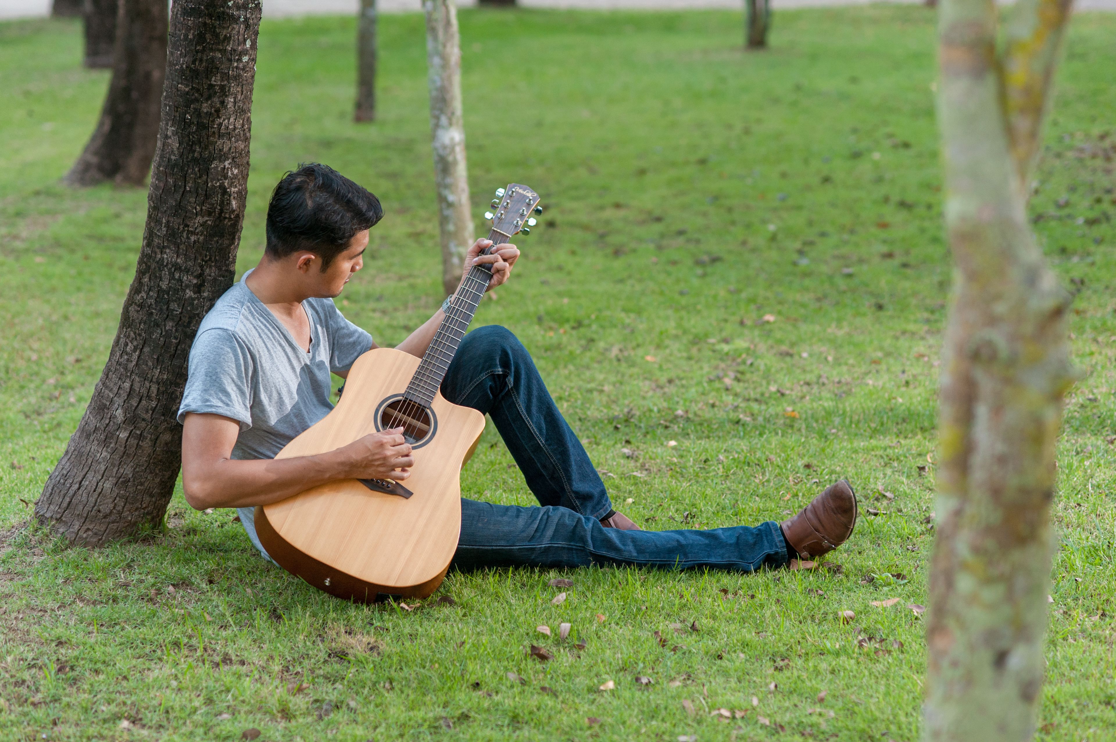 Iemand zit op het gras en speelt op een gitaar.