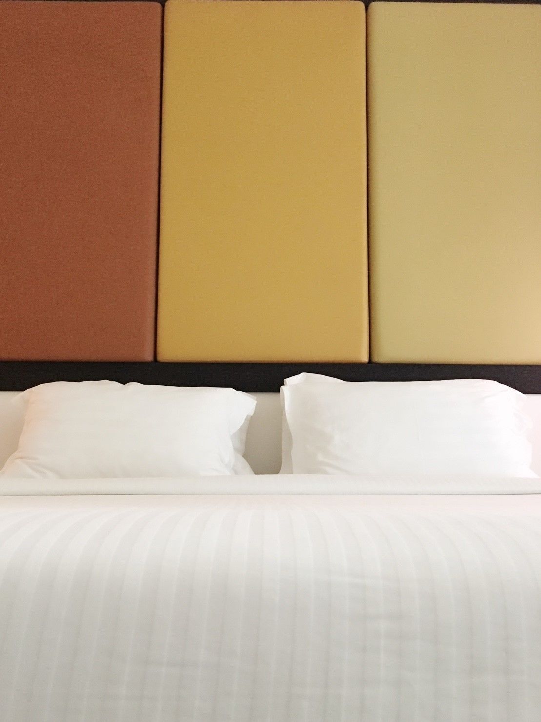 A hotel room with a bed, white bedding, and a headboard with three panels in different colors.