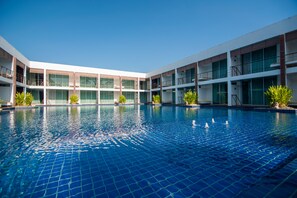 Um hotel moderno com uma grande piscina interna, várias varandas e um céu azul límpido.
