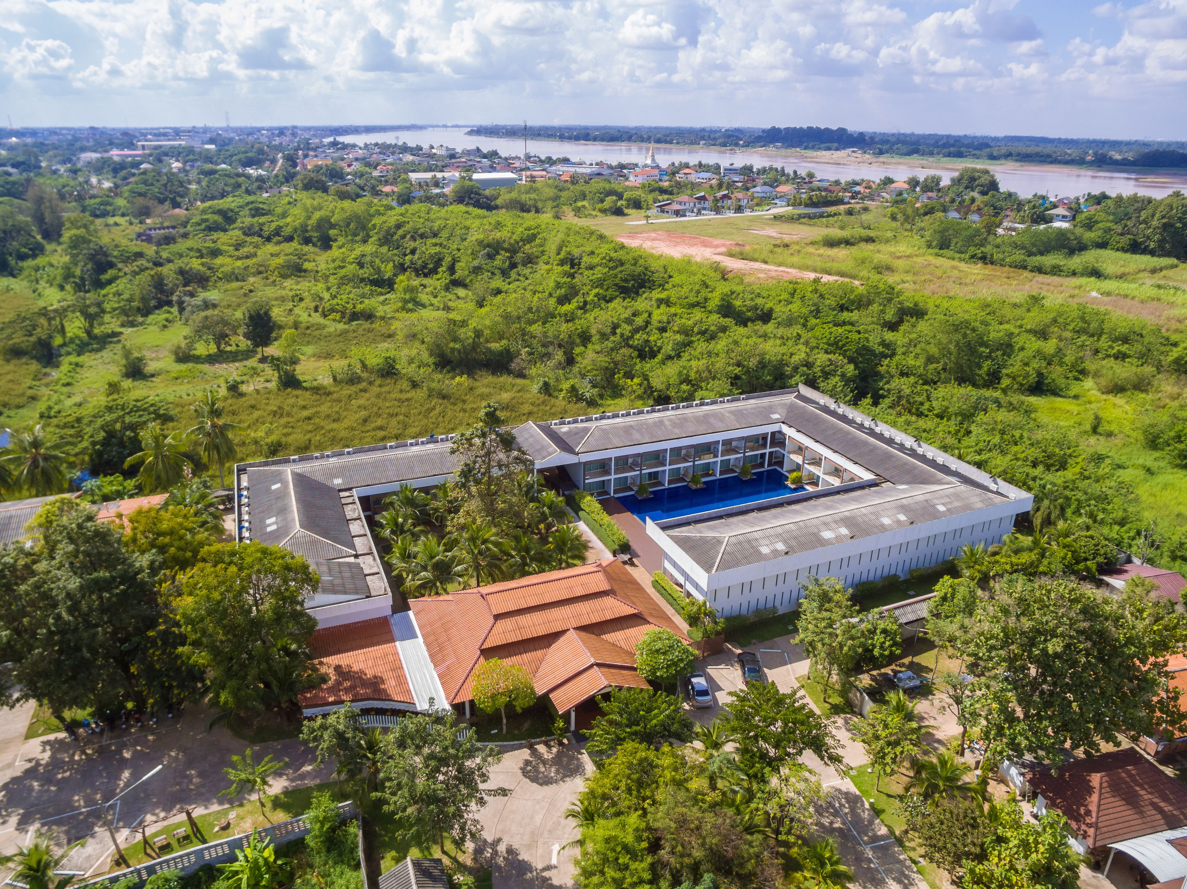 An aerial view of a hotel with a swimming pool, surrounded by lush greenery and a river in the background.