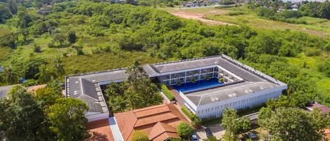 An aerial view of a hotel with a swimming pool, surrounded by lush greenery and a river in the background.