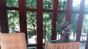 Un coin salon avec un fauteuil en osier, une petite table ornée d’un vase de fleurs et une table d’appoint en bois sur laquelle est posée une plante en pot.