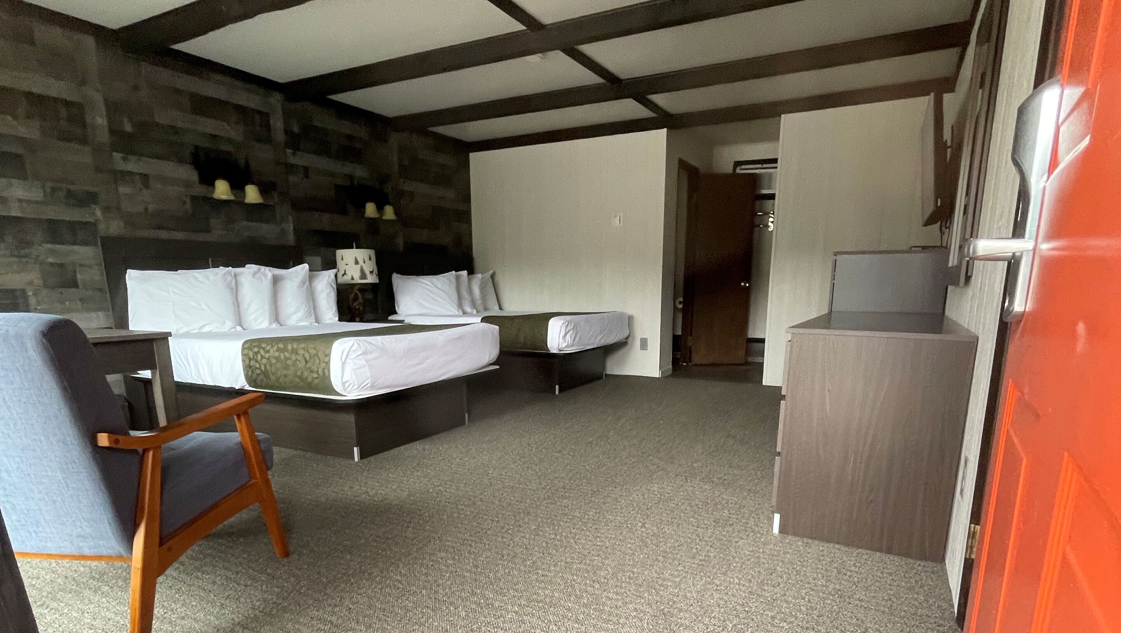 A hotel room with a bed, a desk, a chair, and a kitchenette.