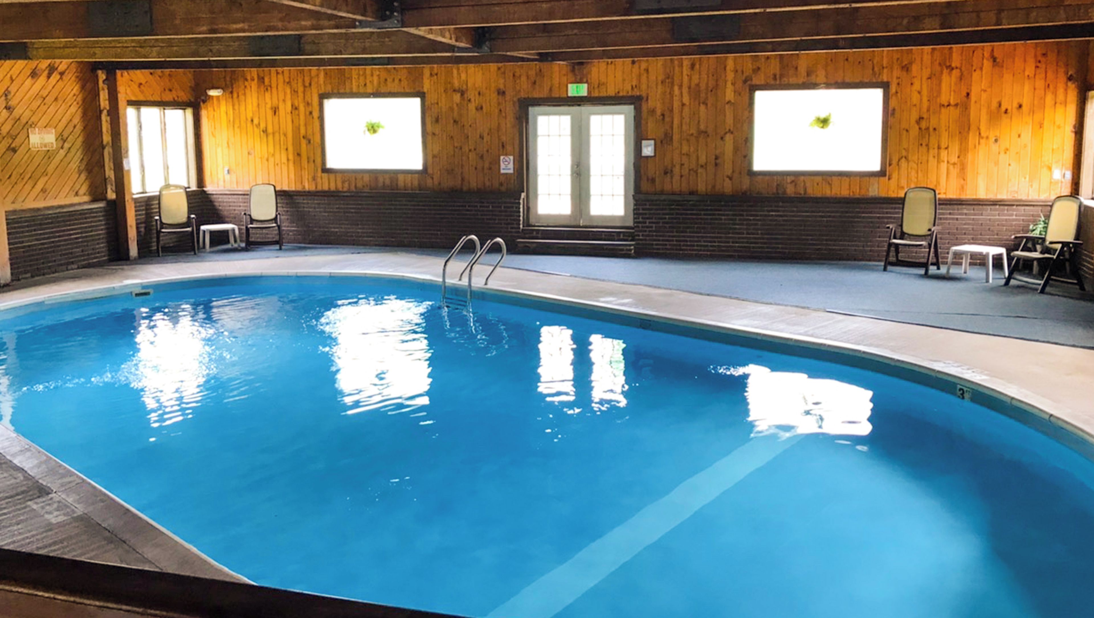 An indoor swimming pool with a wooden interior, a diving board, and chairs around the pool area.