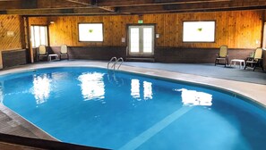 An indoor swimming pool with a wooden interior, a diving board, and chairs around the pool area. - Adirondack Lodge Old Forge (Thendara)