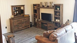 A living room with a wooden entertainment center, a television, a brown leather sofa, and a wooden dresser with drawers. - Adirondack Lodge Old Forge (Thendara)