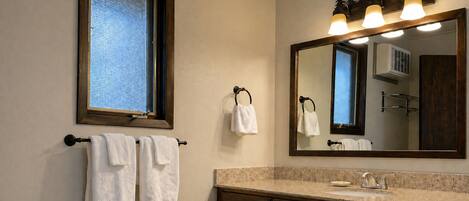 A bathroom with a window, a mirror, a sink, and a towel rack.