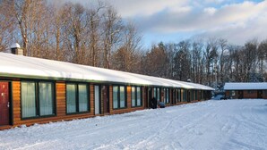 A row of log cabins with snow-covered roofs, surrounded by trees. - Adirondack Lodge Old Forge (Thendara)