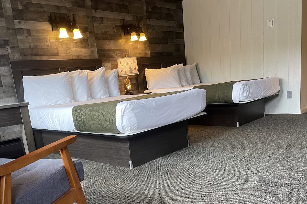 A double bed with a wooden headboard, a bedside table, a lamp, and a chair in a room with a herringbone-patterned wall.