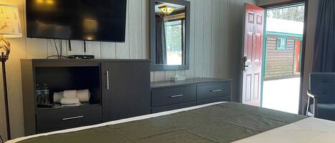Une chambre d’hôtel équipée d’un lit, d’une télévision, d’un miroir, d’une armoire et d’une porte donnant sur l’extérieur.