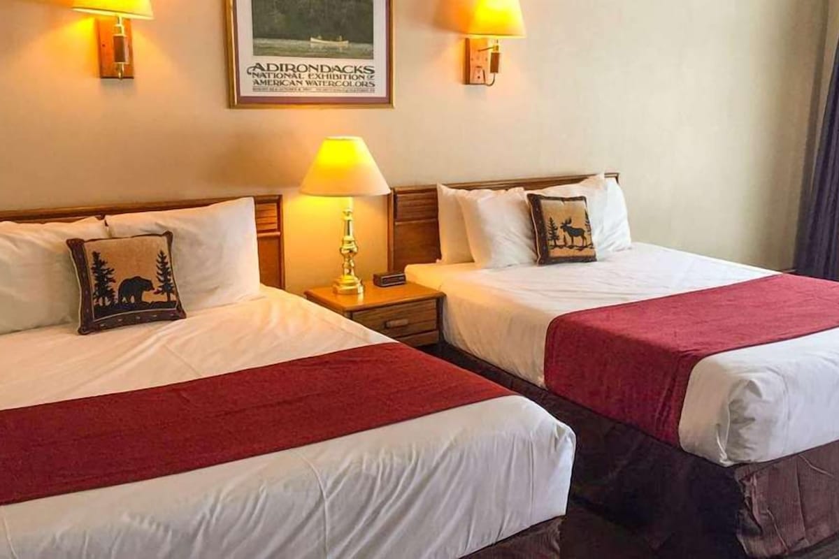 A hotel room with two beds, each with a red blanket, bedside lamps, and a framed picture on the wall.