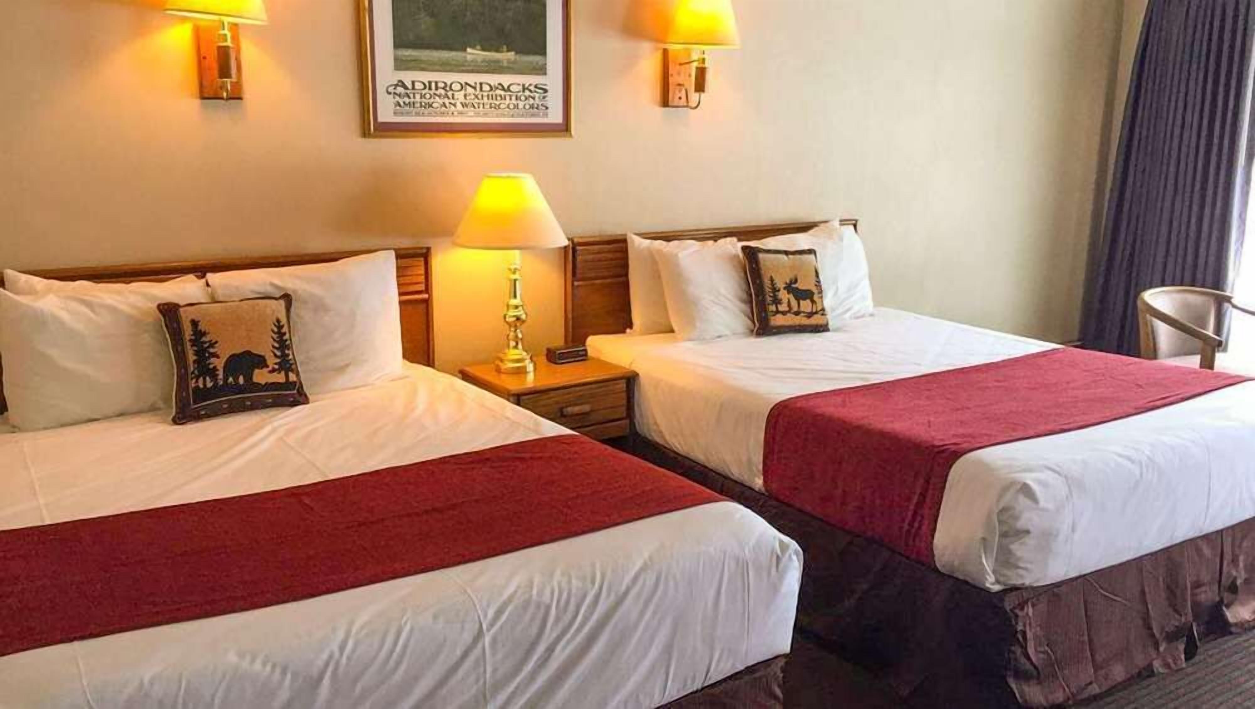 Een hotelkamer met twee bedden, elk met een rode deken, nachtlampjes en een ingelijste foto aan de muur.