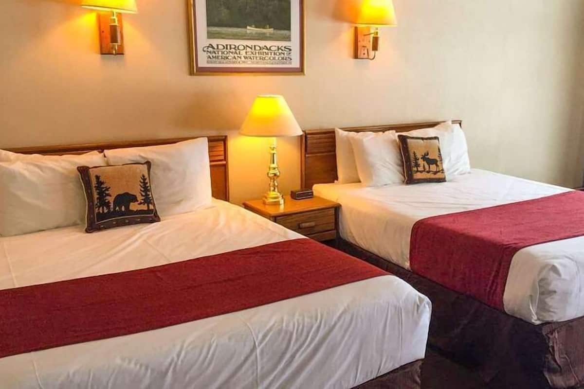 A hotel room with two beds, each with a red blanket, bedside lamps, and a framed picture on the wall.