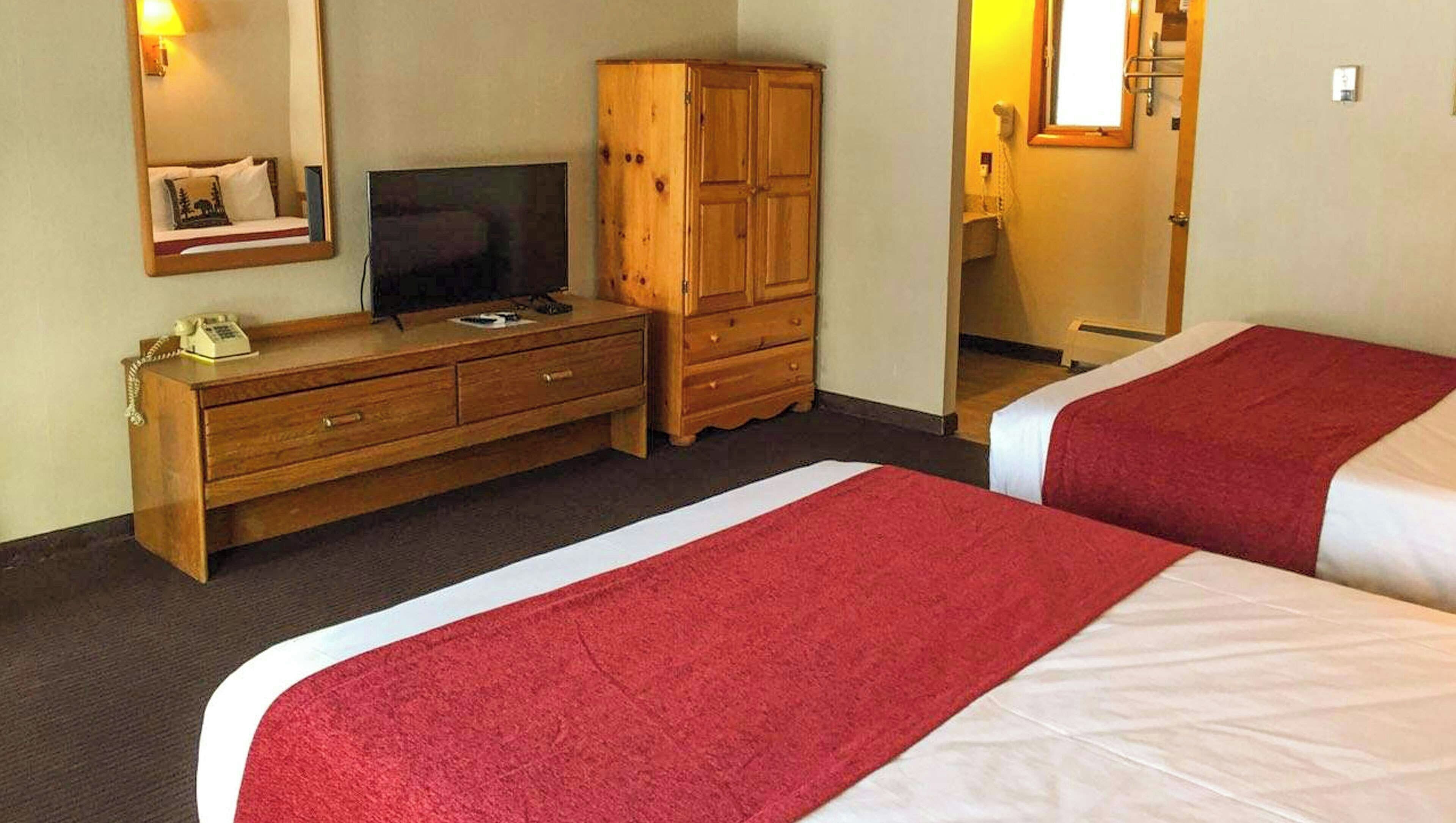 Une chambre d’hôtel avec deux lits, une commode en bois, une télévision et un miroir.