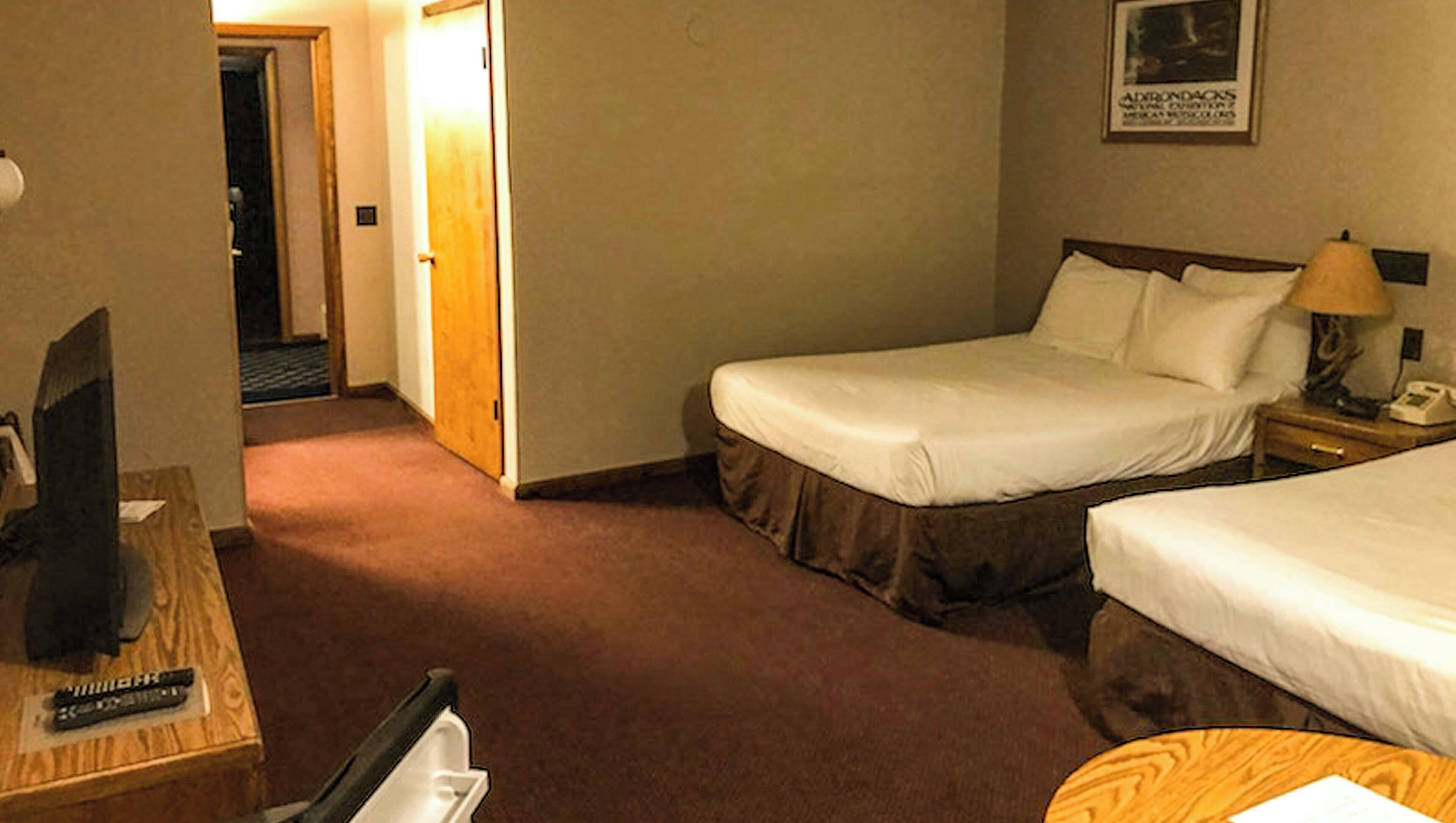 A hotel room with two beds, a desk with a television, a lamp, and a framed picture on the wall.