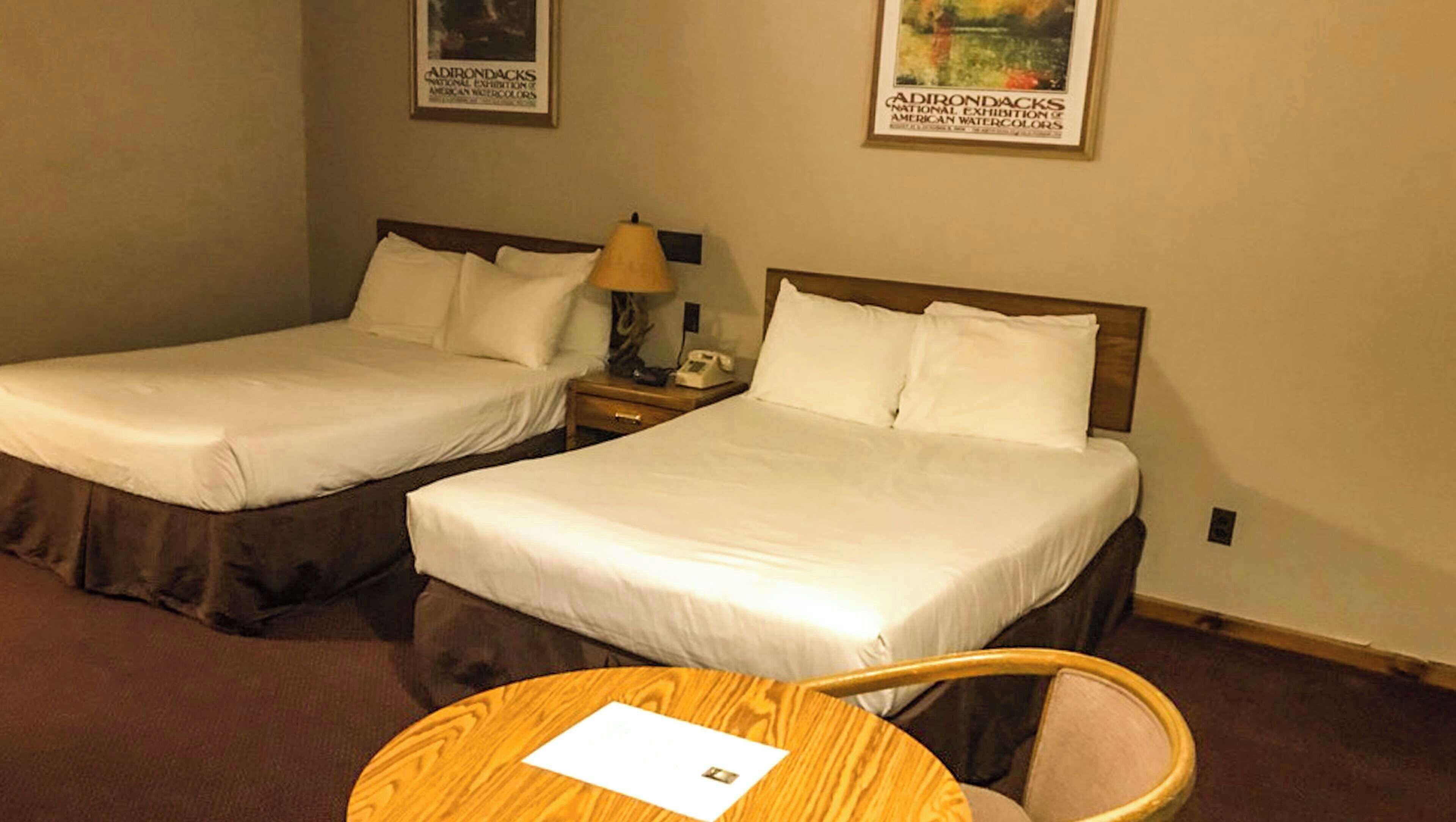 Habitación de hotel con dos camas, una mesa redonda de madera y una silla. En la pared, hay carteles enmarcados.