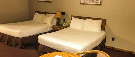 Habitación de hotel con dos camas, una mesa redonda de madera y una silla. En la pared, hay carteles enmarcados.