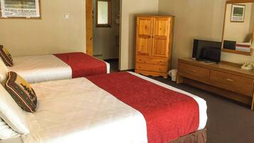 A hotel room with two beds, a wooden wardrobe, a television, and a mirror.