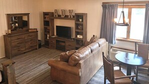 A living room with a fireplace, wooden furniture, a leather sofa, and a dining table with chairs. - Adirondack Lodge Old Forge (Thendara)