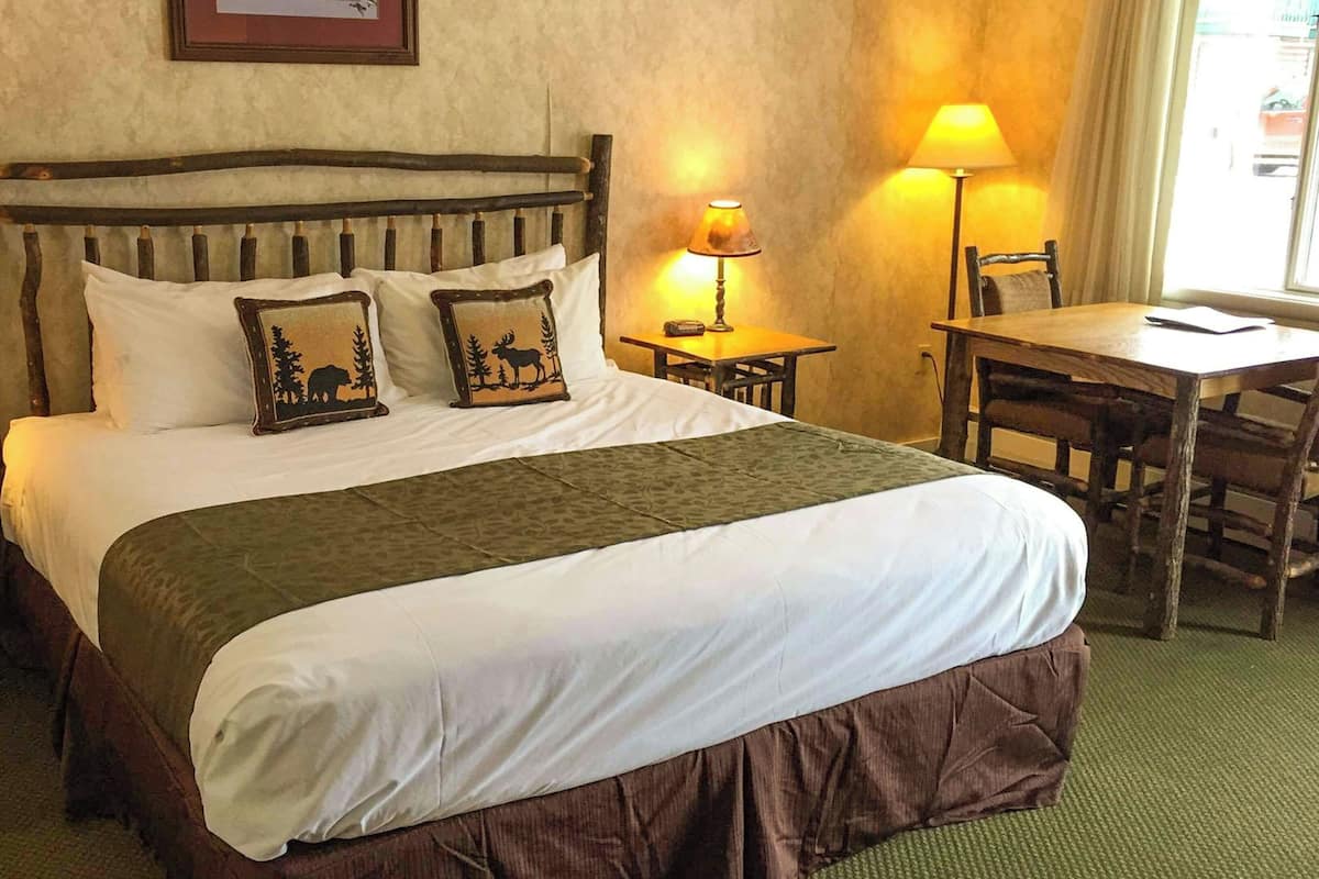 A bed with a wooden headboard, two bedside tables with lamps, a chair, and a small table with a lamp.