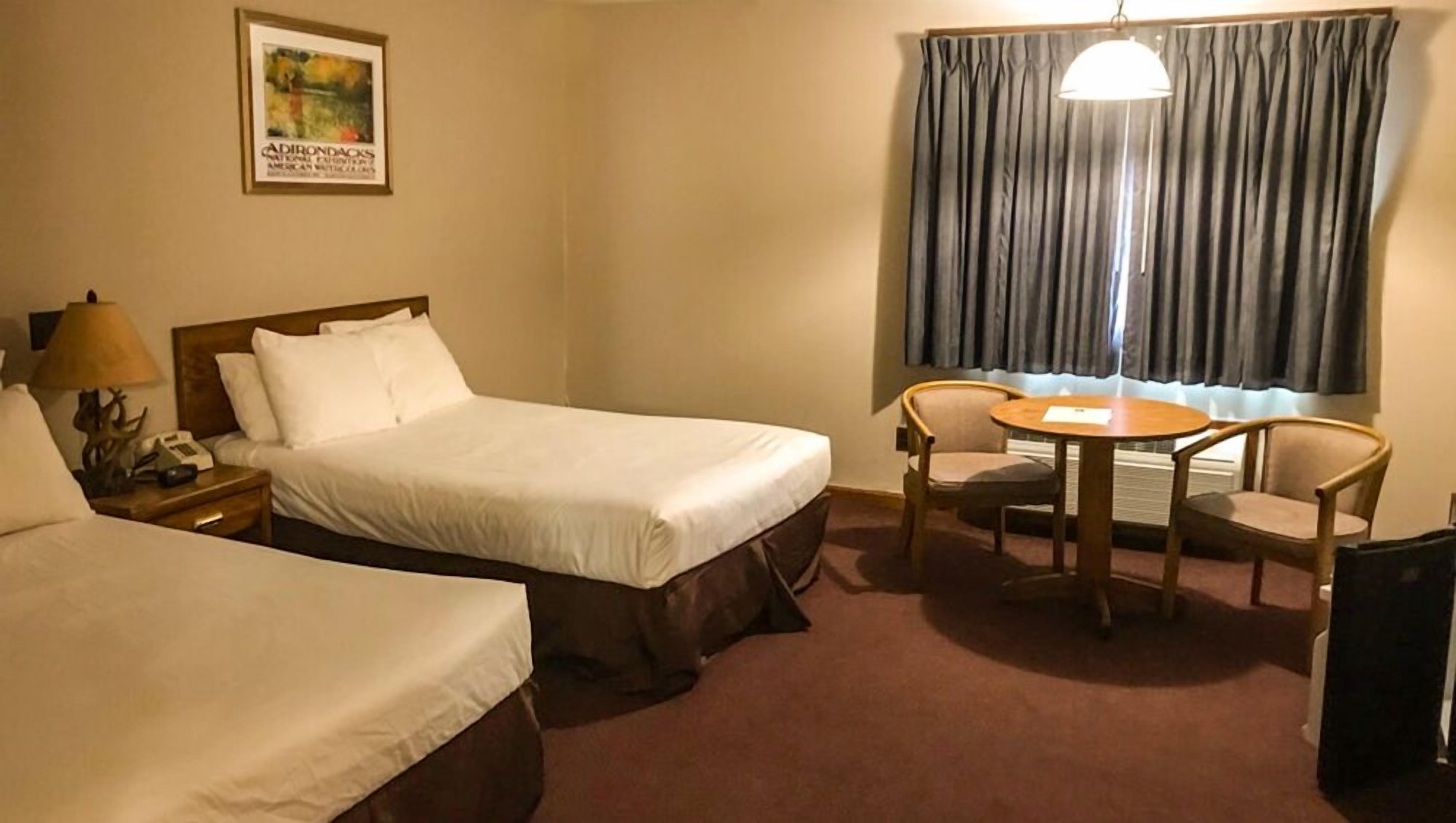 Een hotelkamer met twee bedden, een tafel met stoelen, een lamp, een telefoon en een raam met gordijnen.