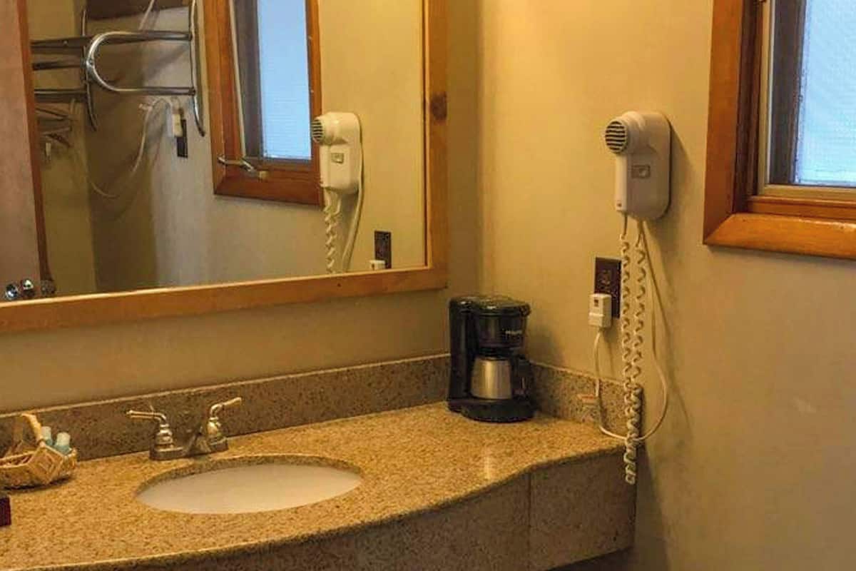 A bathroom with a sink, a hair dryer, a coffee maker, and a mirror.