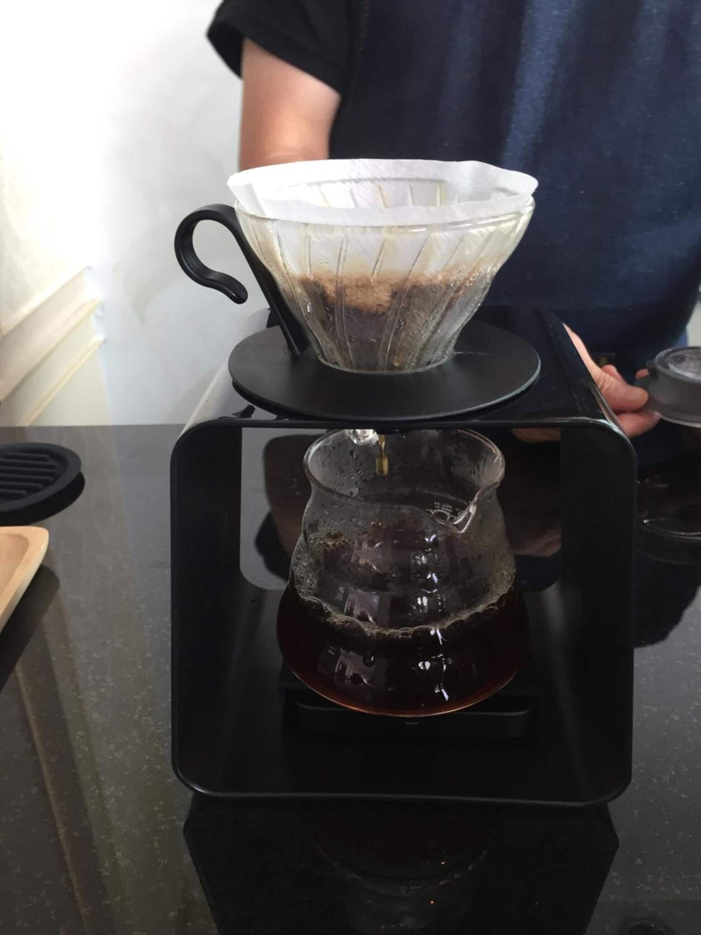 Een koffiezetapparaat met een filter en een glazen kan op een zwart dienblad.