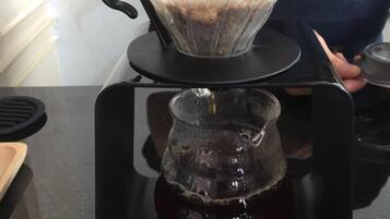Een koffiezetapparaat met een filter en een glazen kan op een zwart dienblad.