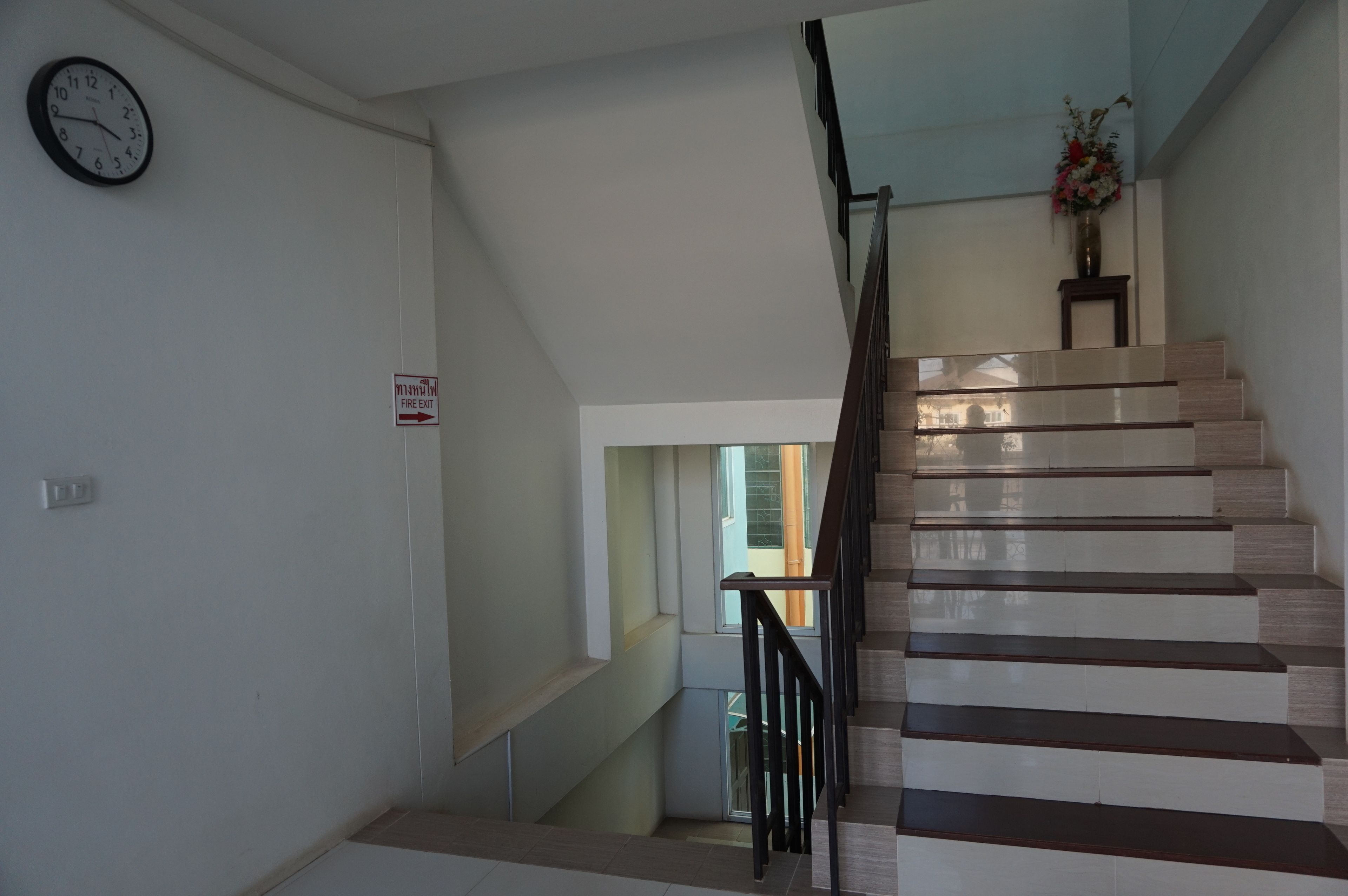 Una escalera con barandilla, un reloj y un letrero de salida de incendios en la pared.