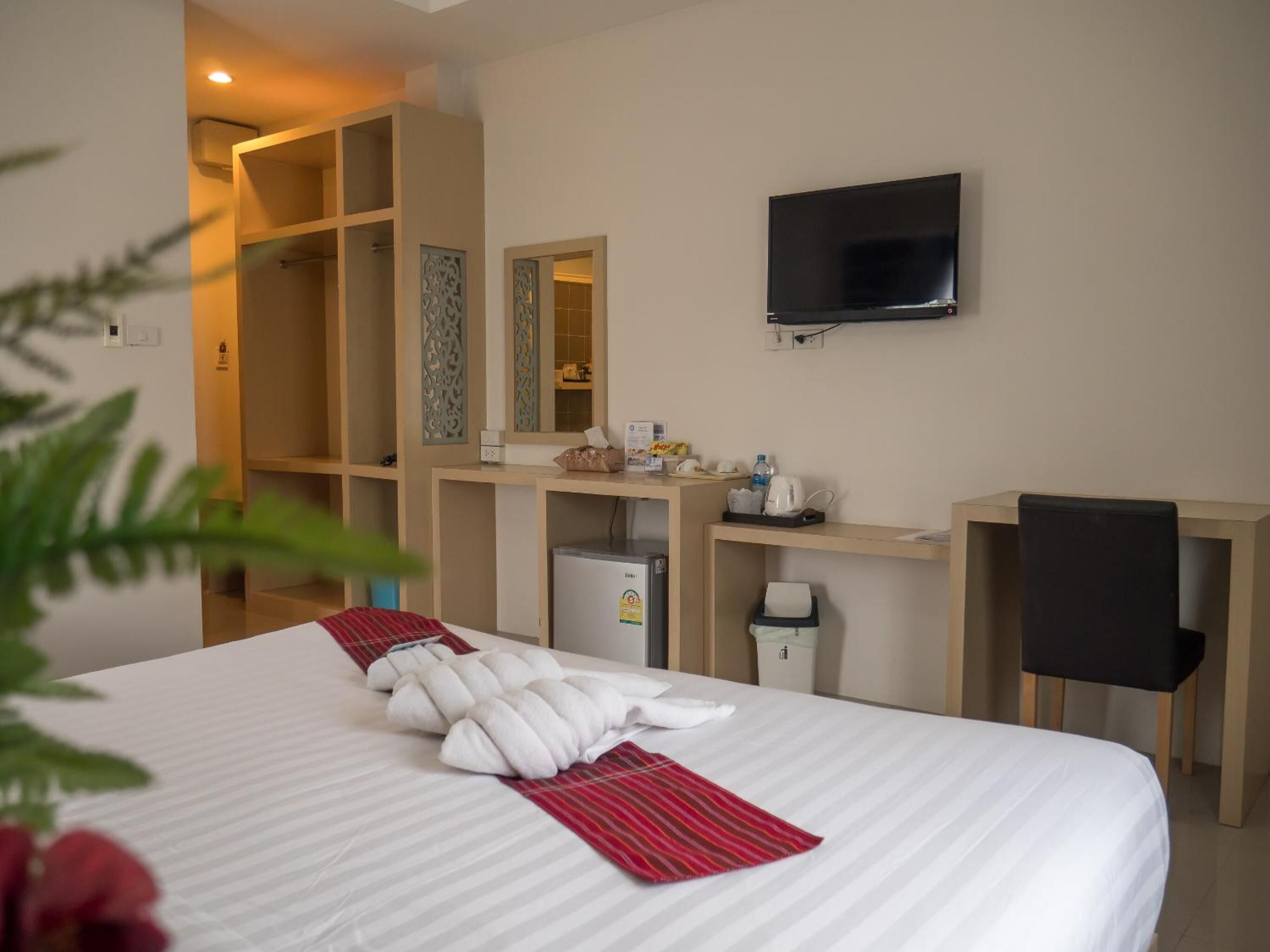 A hotel room with a bed, a desk, a chair, a TV, and a minibar.