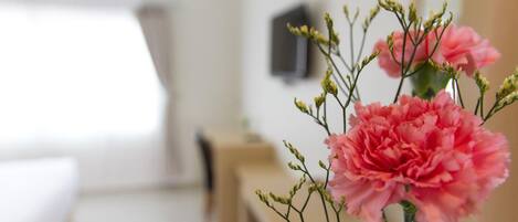 Una habitación con una cama, una mesita de noche y un jarrón con flores rosadas.