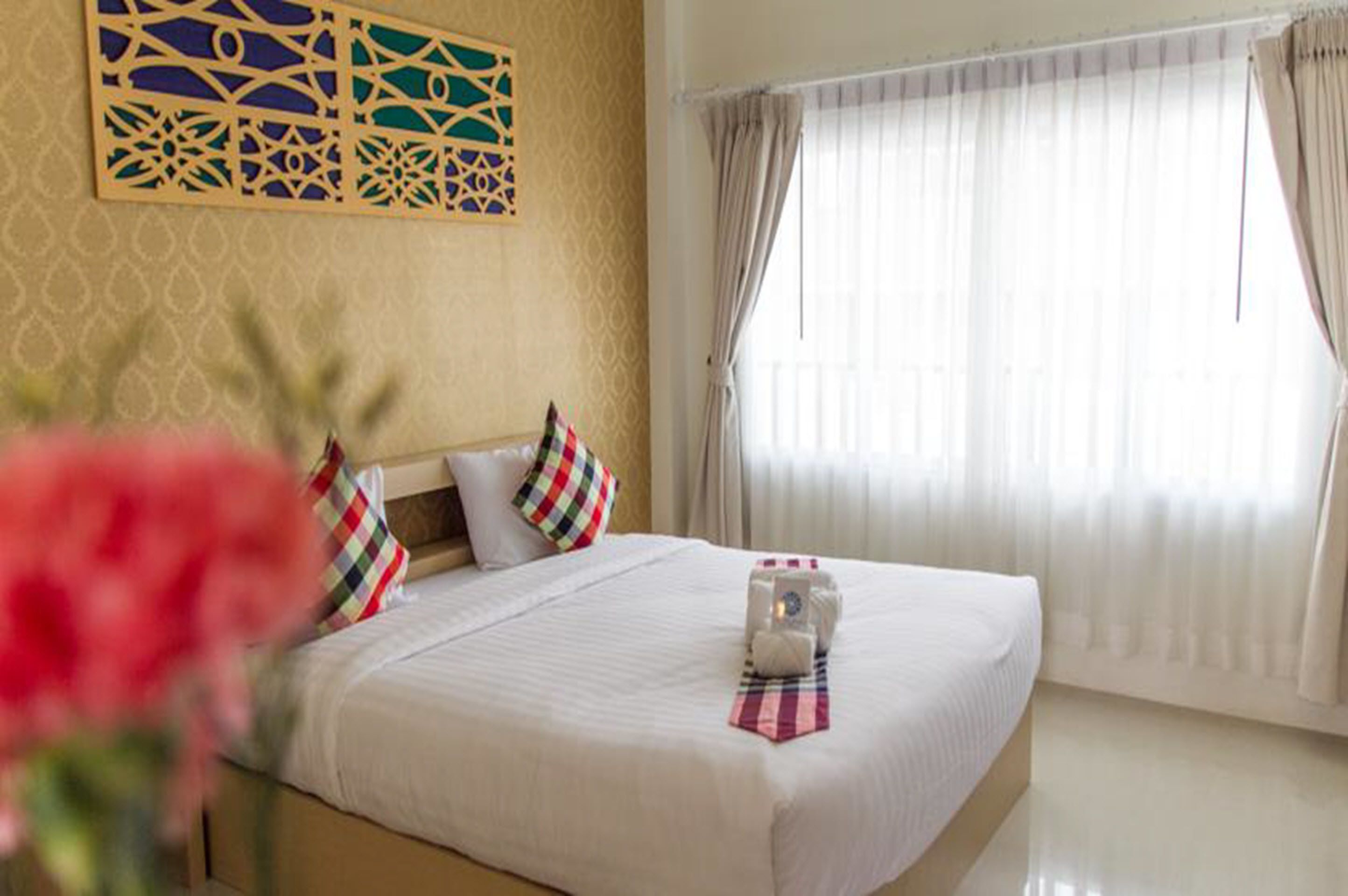 Una habitación de hotel con una cama grande, un panel decorativo en la pared y cortinas de gasa.
