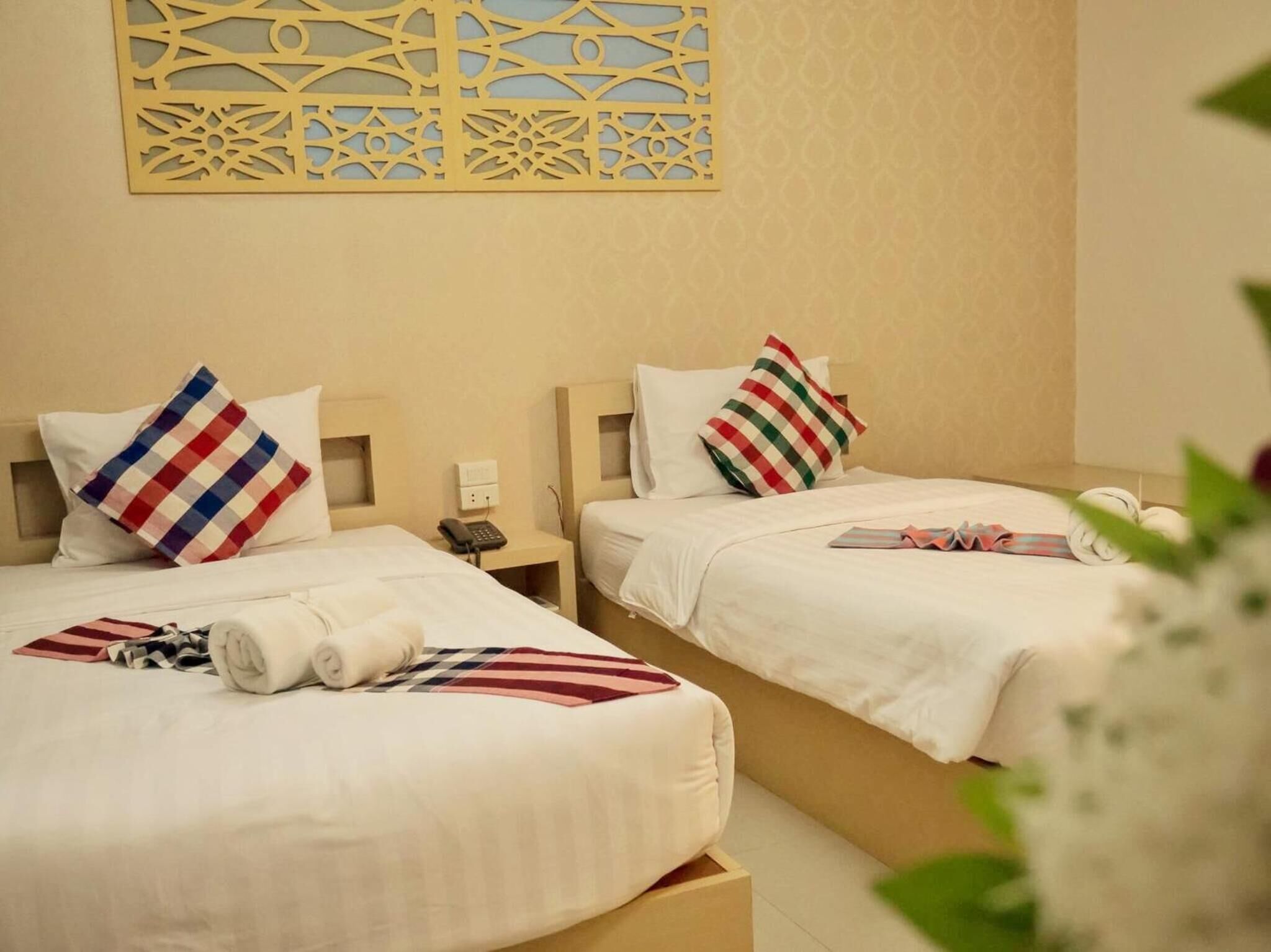 A hotel room with two beds, each with a pillow, a bedside table with a phone, and a decorative wall panel.