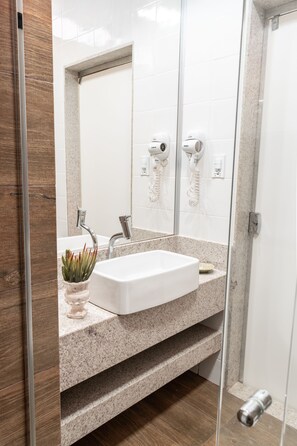 A modern bathroom with a white sink, granite countertop, and a glass shower enclosure. - BellaMinas Pousada (Guape)