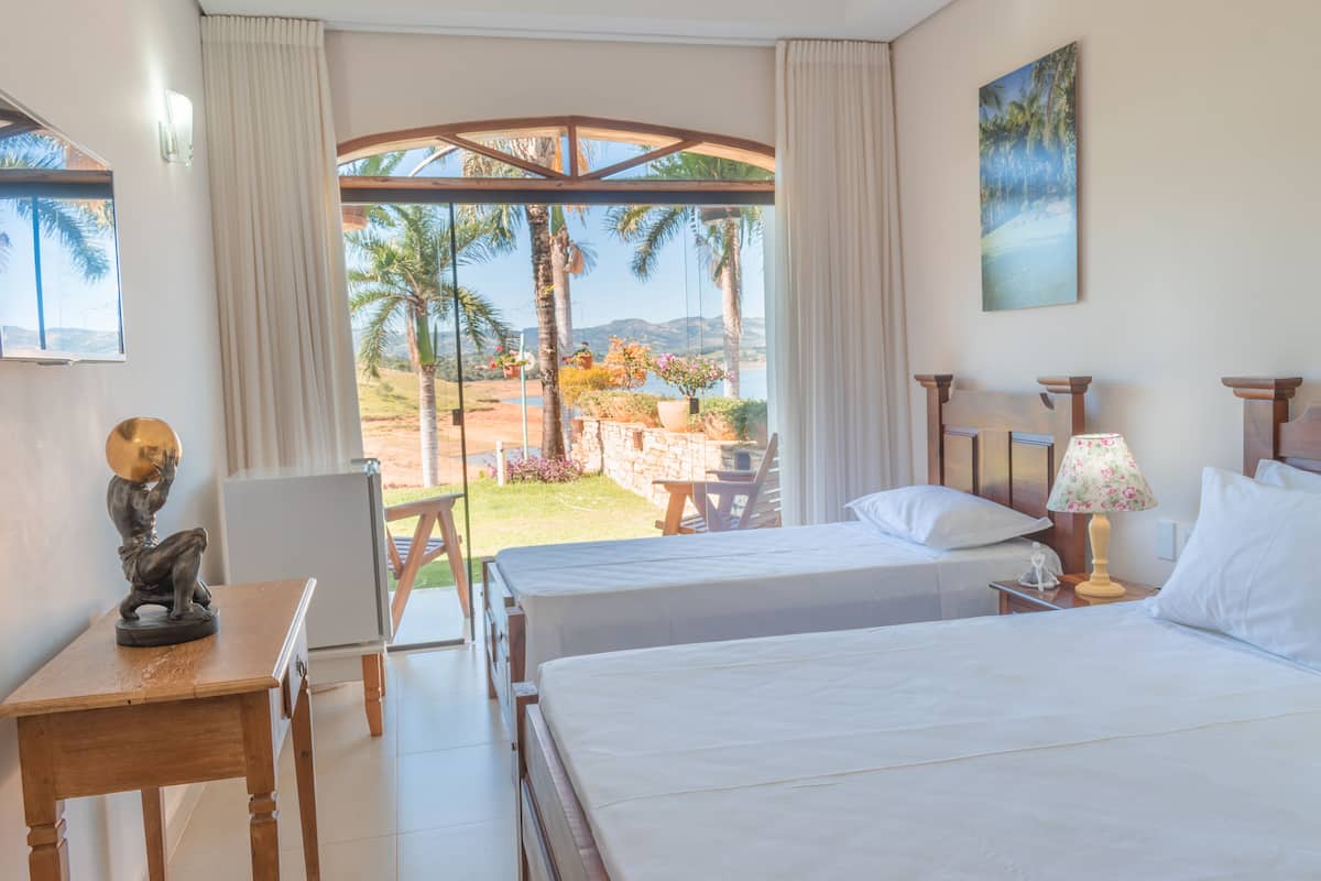 A hotel room with two beds, a desk, and a view of palm trees and mountains.