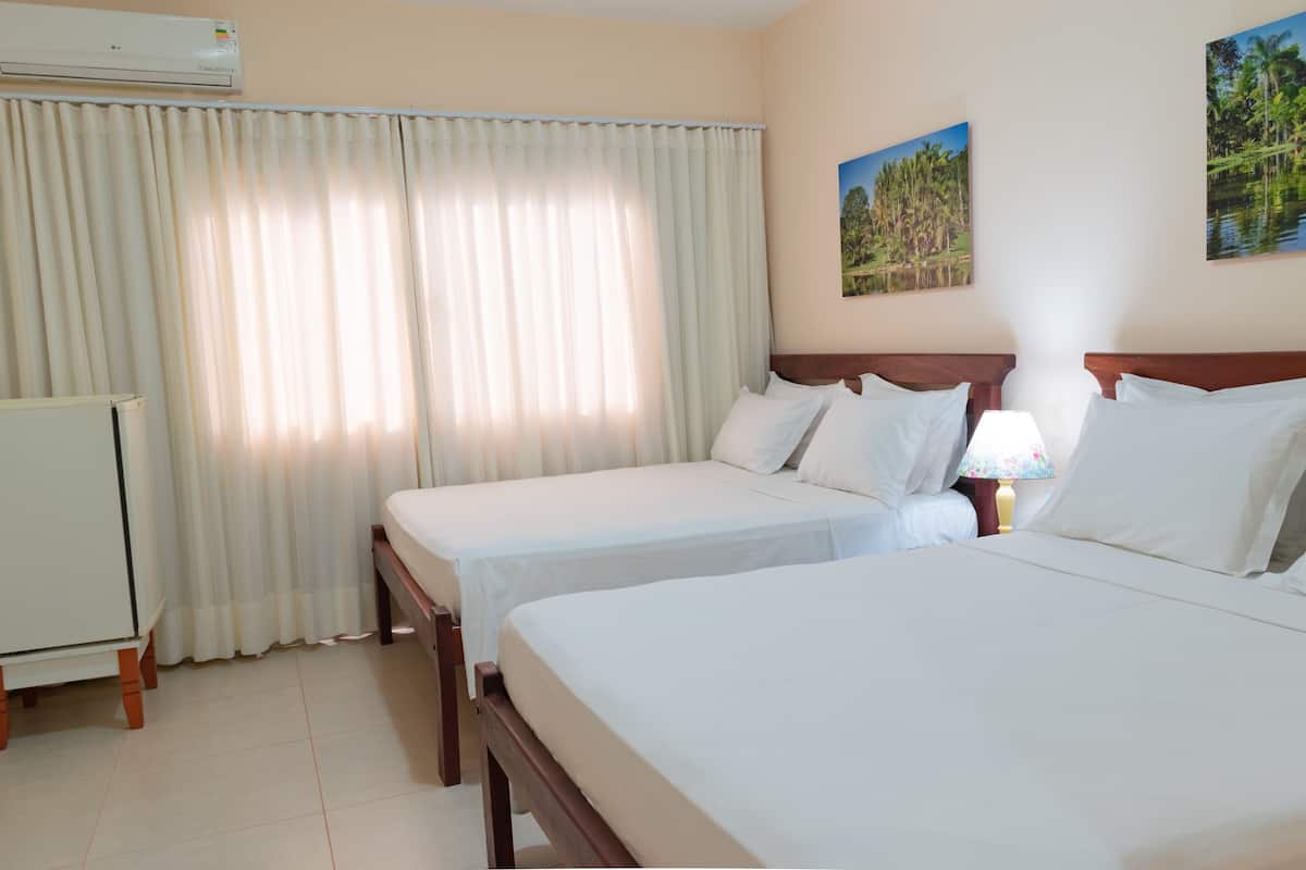 A hotel room with two beds, a desk, an air conditioner, and a lamp.