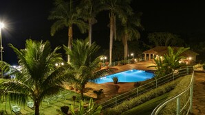 Une vue nocturne d’un complexe hôtelier avec une piscine, des palmiers et un espace détente bien éclairé.