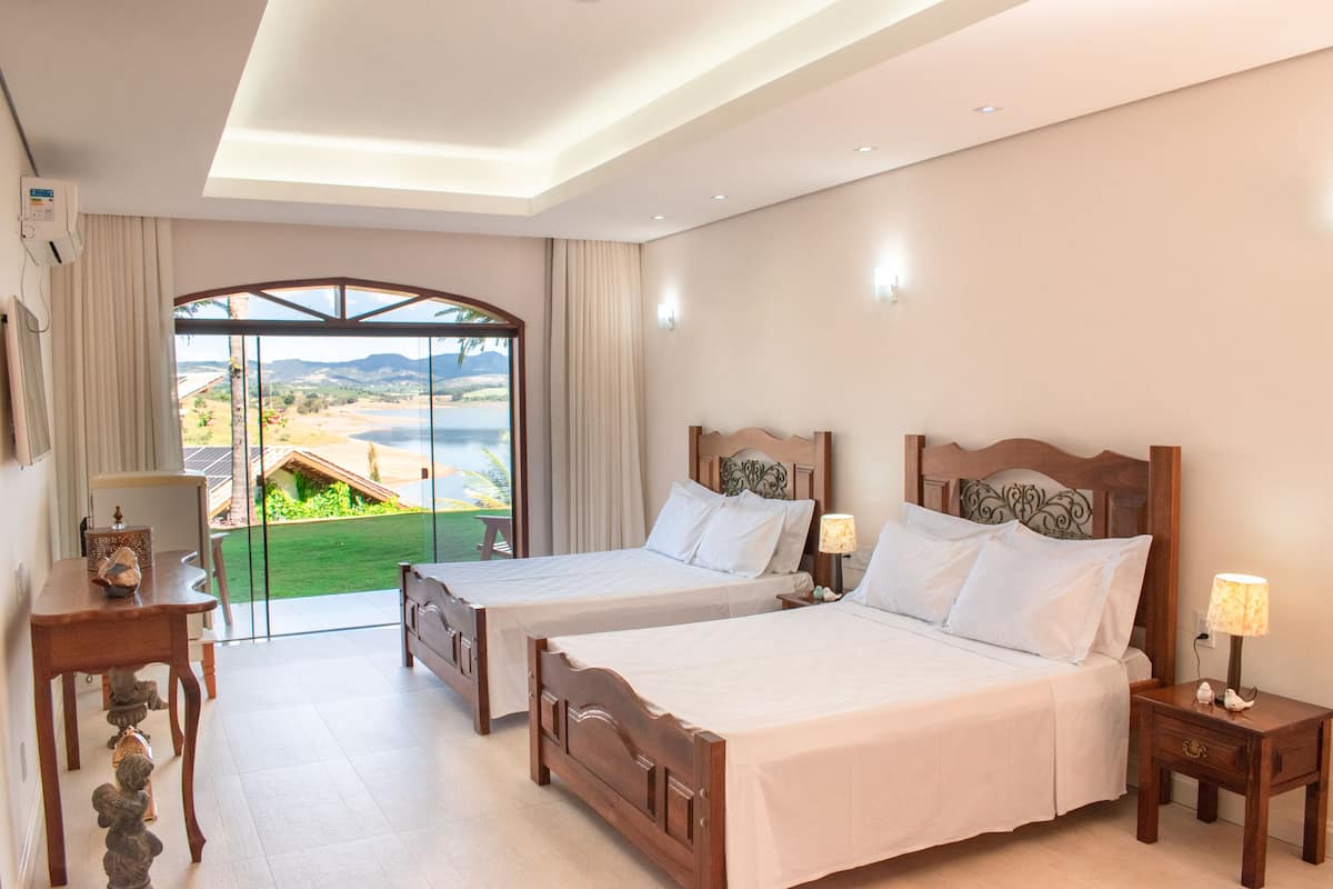A hotel room with two beds, a desk, and a view of a coastal landscape.