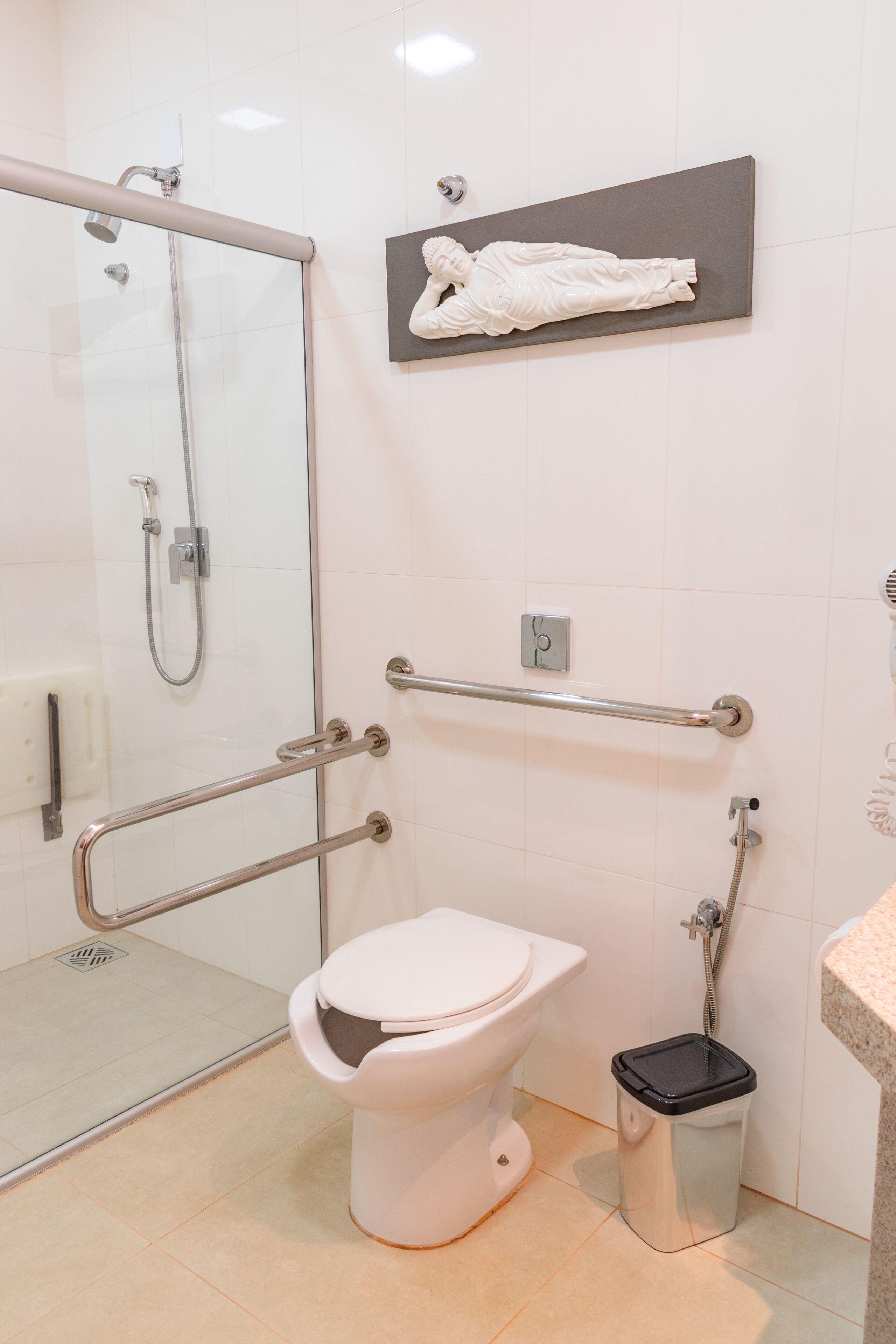 A bathroom with a glass shower enclosure, a white toilet, a black trash bin, and a wall-mounted handrail.