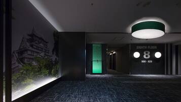 A hallway with a traditional building mural, a green wall, and a sign indicating the eighth floor with a phone number.