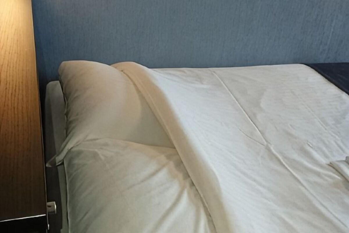 Una cama con sábanas blancas, cabecera de madera y pared azul.