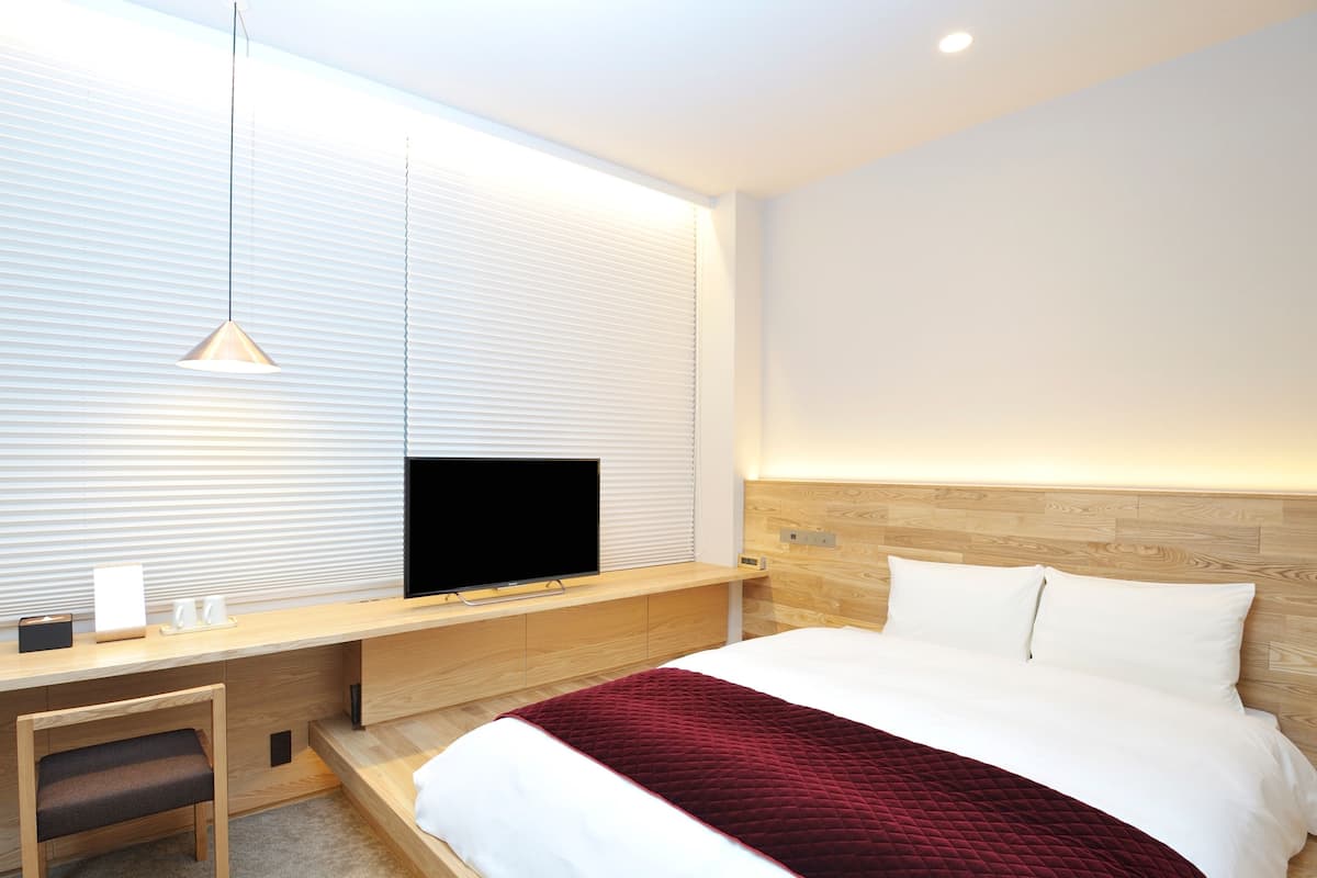 Una habitación de hotel moderna con un escritorio de madera, un televisor de pantalla plana, una cama con ropa blanca y una colcha acolchada roja.