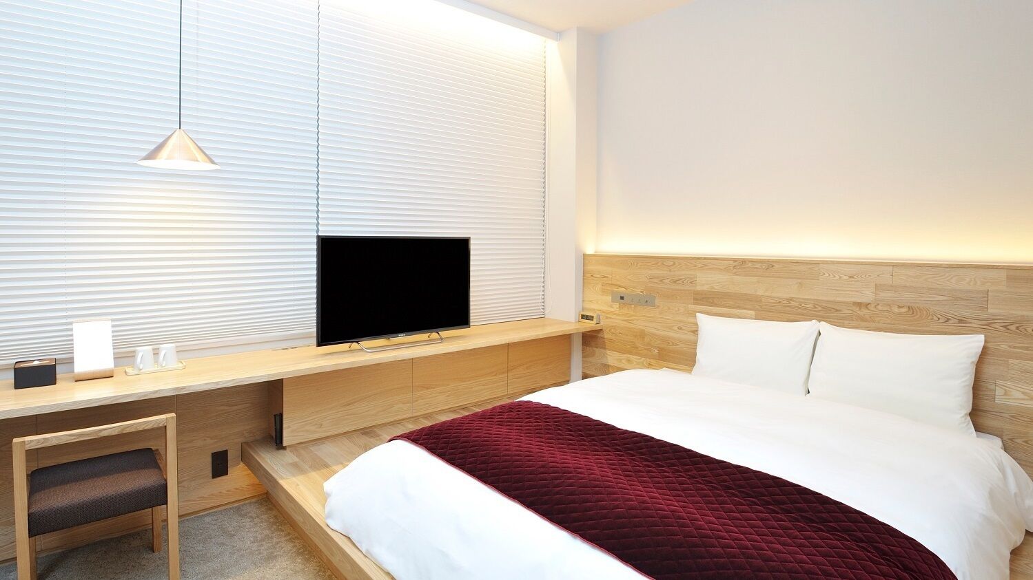 Een moderne hotelkamer met een bed, een bureau met een televisie en een raam met zonwering.