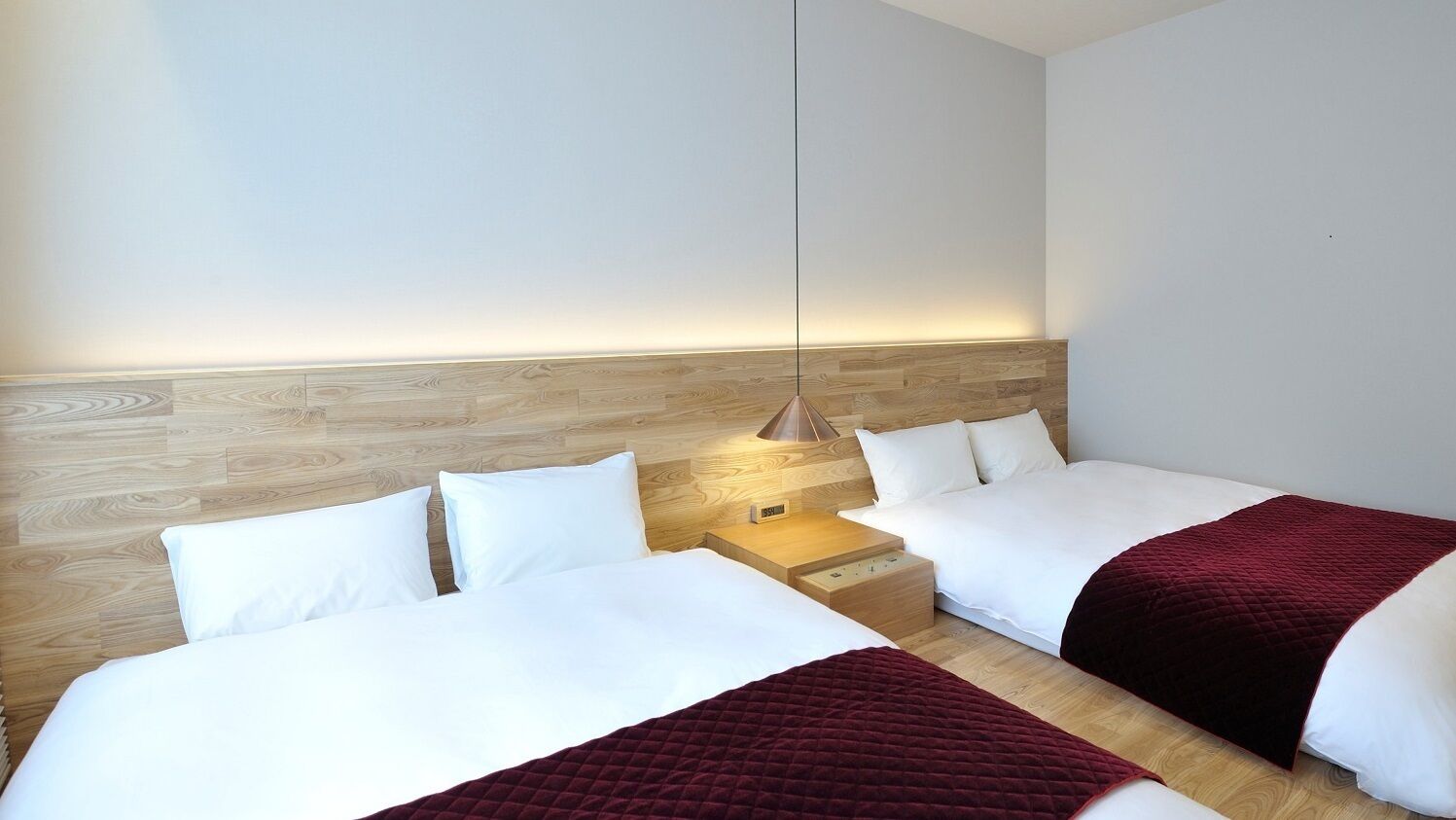 Een hotelkamer met twee bedden, een houten hoofdeinde, een nachtkastje met lamp en een wandlamp.
