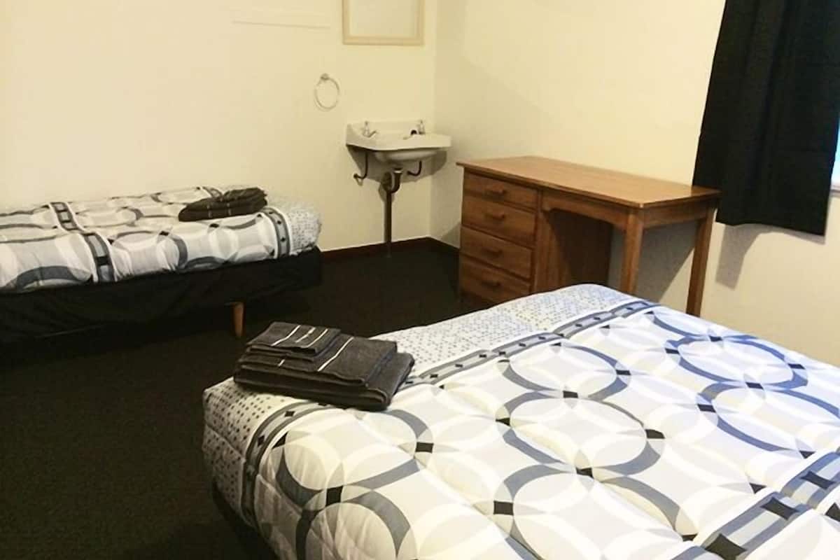 A hotel room with two beds, a wooden desk, a small sink, and a framed picture on the wall.
