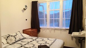Een slaapkamer met een bed, een nachtkastje, een raam met gordijnen en een badkamer met een wastafel.