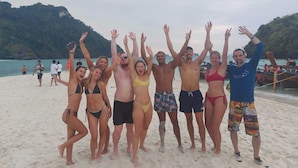 A group of people on a sandy beach with boats in the background. - Sleeper Hostel (Krabi)